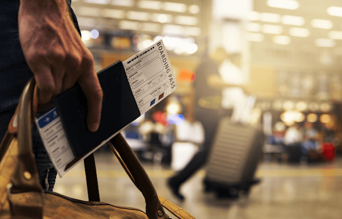 A traveller holding a boarding pass and luggage at an airport, representing the thousands of Kiwis who park at Auckland Airport every month and need to ensure their car insurance covers theft and damage while they are away.