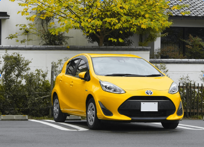 A yellow Toyota Aqua in a parking lot. 