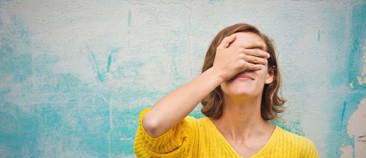 A woman in a yellow shirt with her right hand over her eyes.