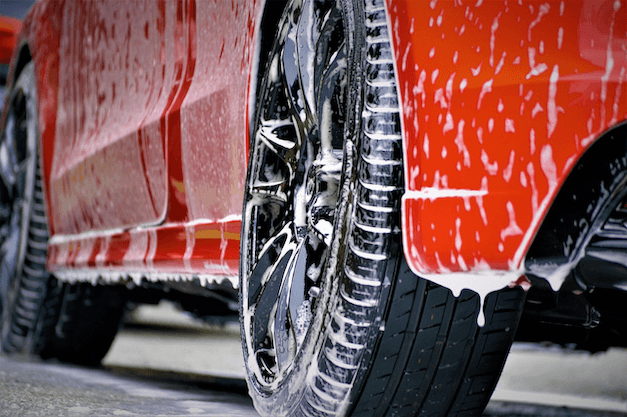 Close-up of a red car wheel covered in soap suds and water during a car wash in New Zealand.