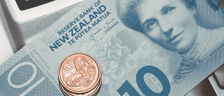 A close-up of a New Zealand ten-dollar banknote with a stack of ten-cent coins resting on top of it.