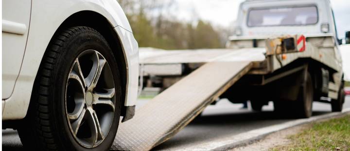 A close-up of a car tyre next to a flatbed tow truck ramp on the side of a New Zealand road.