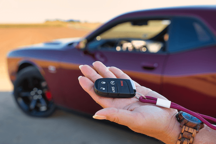 A hand holding a car key fob in front of a vehicle, representing the "handover grey zone" between payment and the formal change of ownership notification to NZTA.