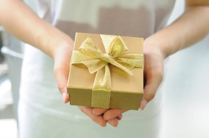 A woman holding a gift wrapped in golden wrapping paper and tied with a golden bow.