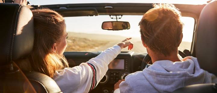 A young couple driving a convertible on a sunny day.