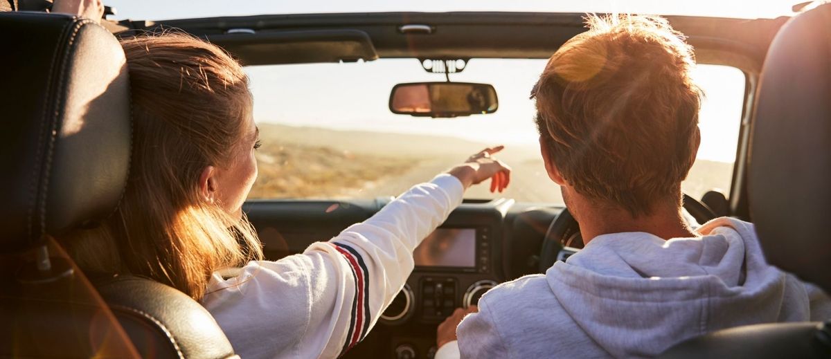 A young couple driving a convertible on a sunny day.