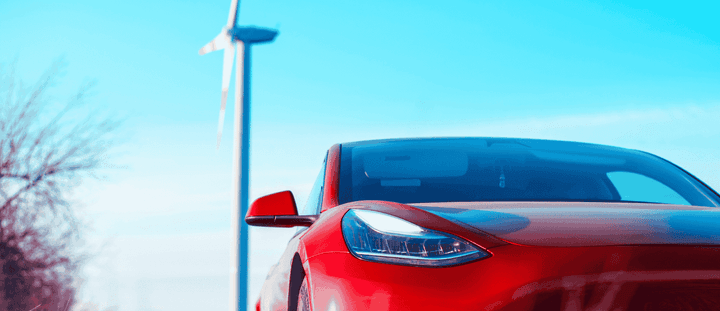 A red electric vehicle parked near a wind turbine.