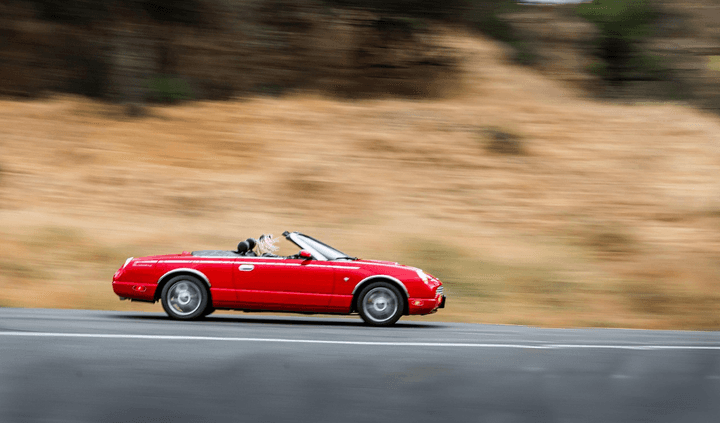 A red car driving along a scenic coastal highway.