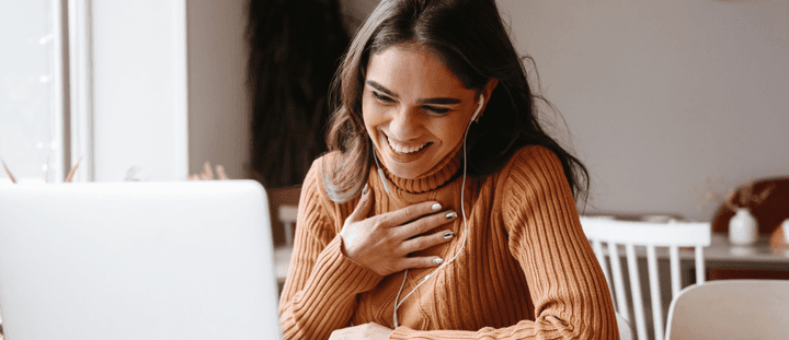 A woman engaged in a conversation on a laptop with headphones in.