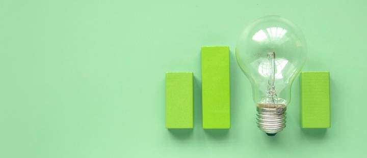 A lightbulb next to green building blocks displayed on a green background.