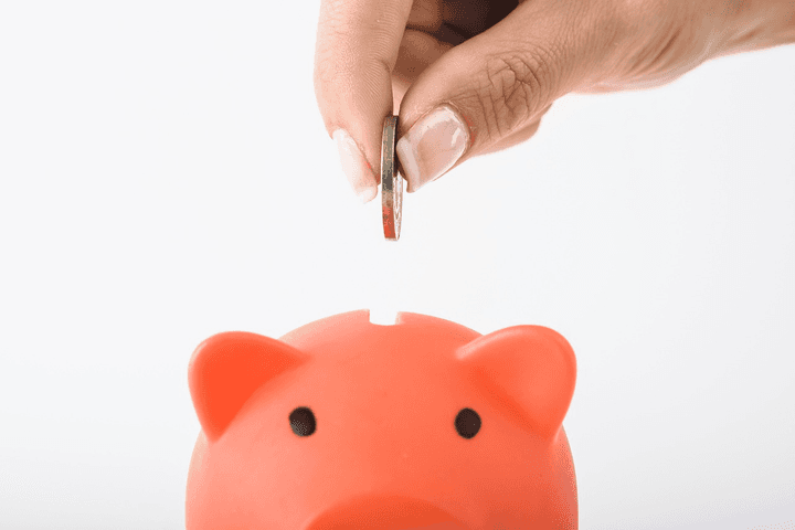 A hand placing a silver coin into a pink piggy bank to represent saving money on 2026 health insurance through a Quashed Market Scan.
