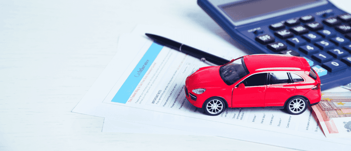A toy car on top of an insurance document alongside a pen and calculator. 