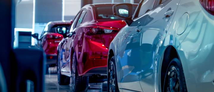 A row of modern cars, including red and blue sedans, parked closely together in a bright dealership showroom, representing vehicle licensing and registration options, featured in this 2026 article by Quashed. 