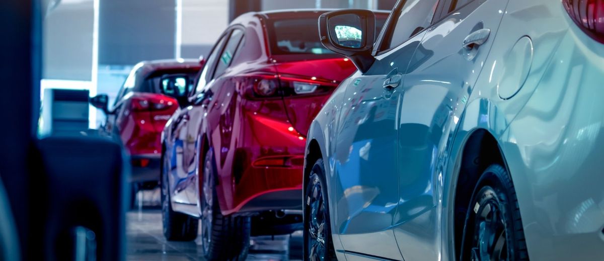 A row of modern cars, including red and blue sedans, parked closely together in a bright dealership showroom, representing vehicle licensing and registration options, featured in this 2026 article by Quashed.