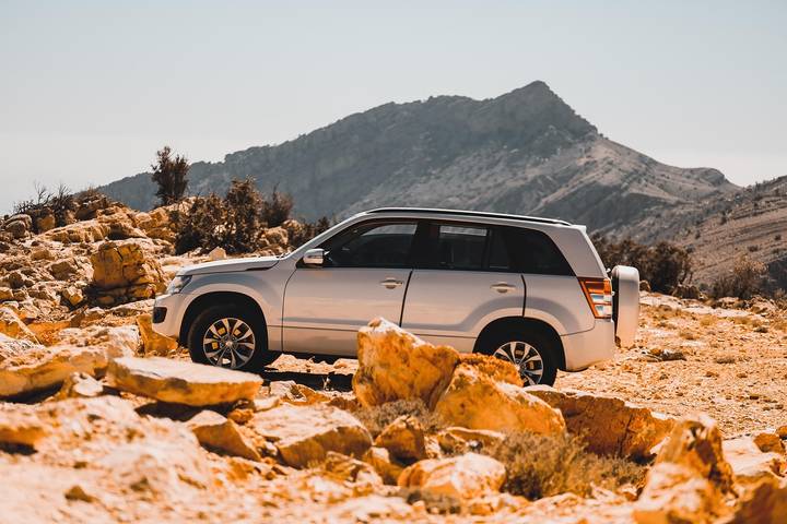 Silver Suzuki Grand Vitara parked on rocky terrain with a mountain backdrop.